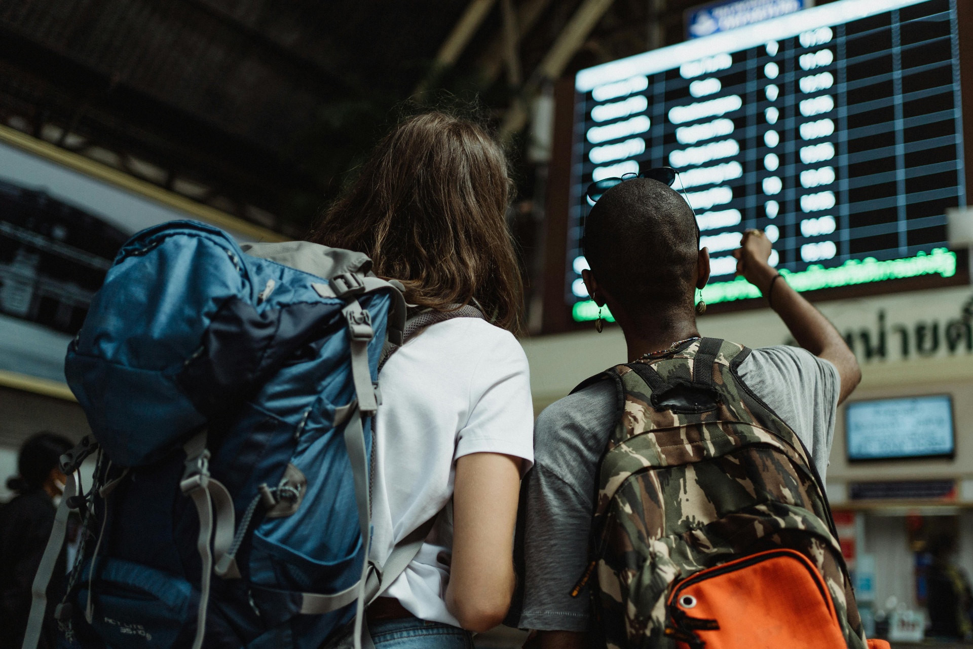 Two backpackers checking the departures board at a train station